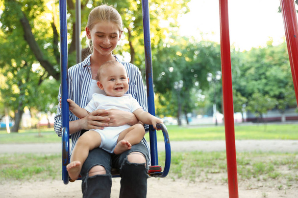 Teen nanny with cute little baby on swing outdoors - Foto, immagini