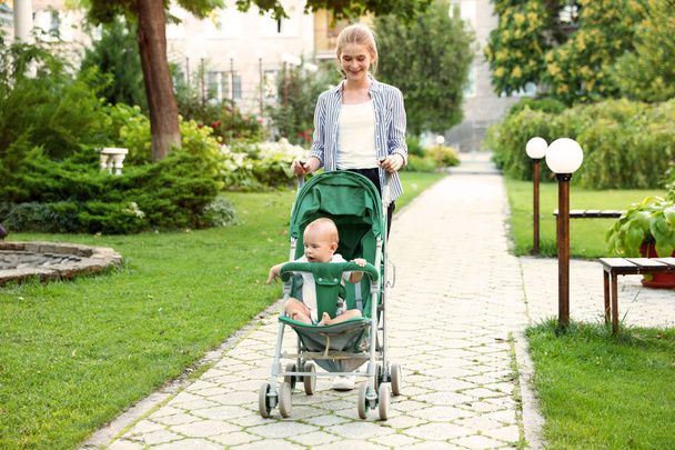 Teen nanny with cute baby in stroller walking in park - Valokuva, kuva