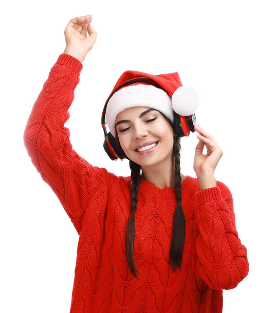 Young woman in Santa hat listening to Christmas music on white background - Foto, Imagem