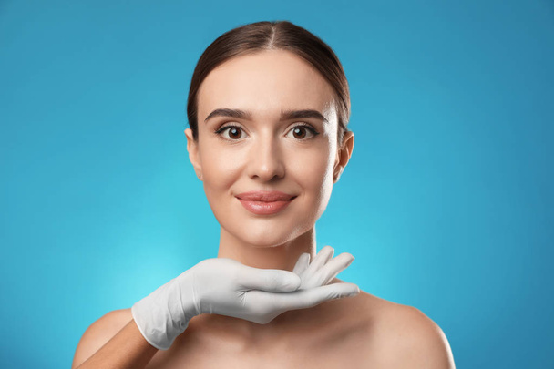 Doctor examining woman's face before plastic surgery on light blue background - Foto, immagini
