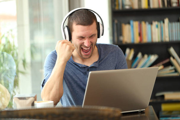Excited man wearing headphones checking laptop - Zdjęcie, obraz