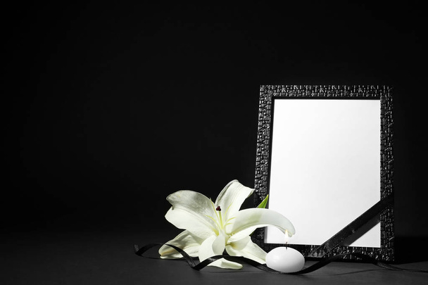 Funeral photo frame with ribbon, white lily and candle on black background. Space for design - Фото, изображение