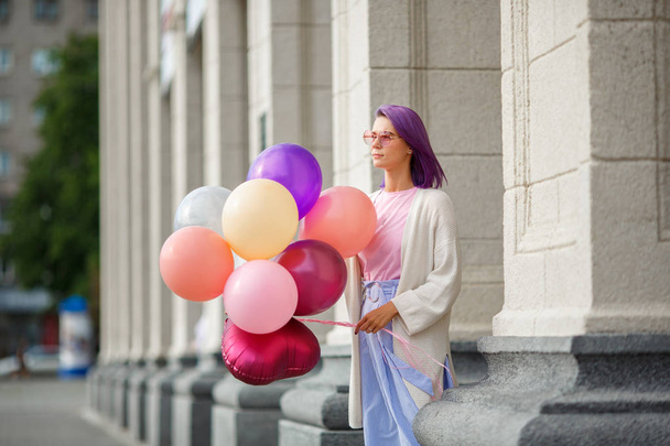 Female with violet hair in pink glasses standing with bunch of baloons - Photo, Image