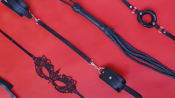 Set for bdsm handcuffs, whip, mask, on a red leather background. - Foto, imagen