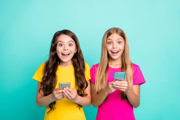 Photo of two fashionable trendy enjoying happy crazy encouraged people wearing yellow pink t-shirts seeing something unreal on screen while isolated with turquoise background - Foto, Imagem
