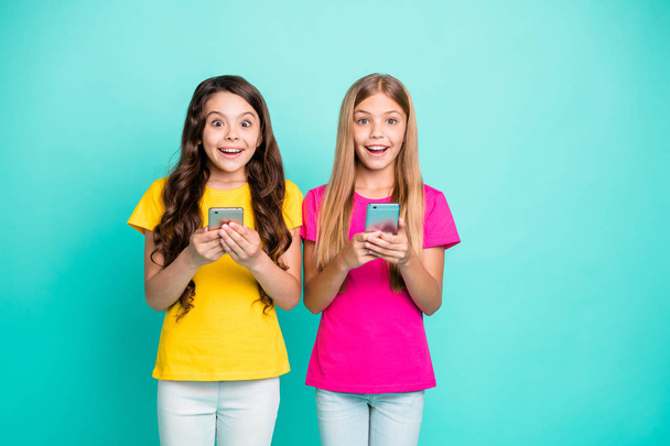 Photo of two people wearing pink yellow t-shirts having been gifted phones rejoicing and shocked with it wearing pink and yellow t-shirts while isolated with teal background - Fotografie, Obrázek