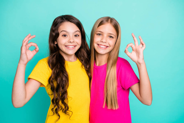 Photo of two smiling girls wearing yellow and pink t-shirts showing you ok sign giving you nice feedback while isolated with teal background - Fotoğraf, Görsel