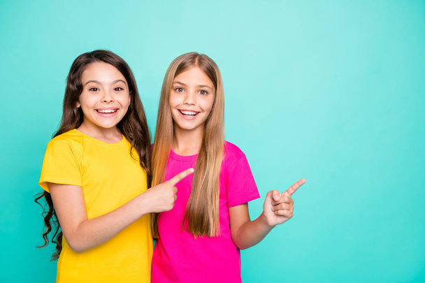 Photo of two casual nice cute girls pointing at place where may be something specified while isolated with teal background - Photo, Image