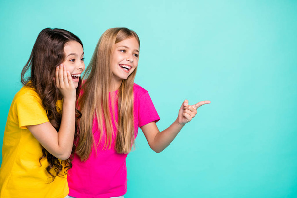 Photo of two nice cute cheerful girls with one of them pointing at emptiness and second being surprised while isolated with teal background with copyspace - Fotó, kép