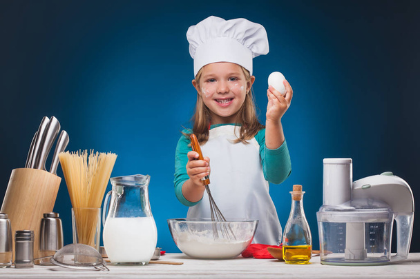Girl Chef prepares a delicious dish on a blue background. - Foto, afbeelding