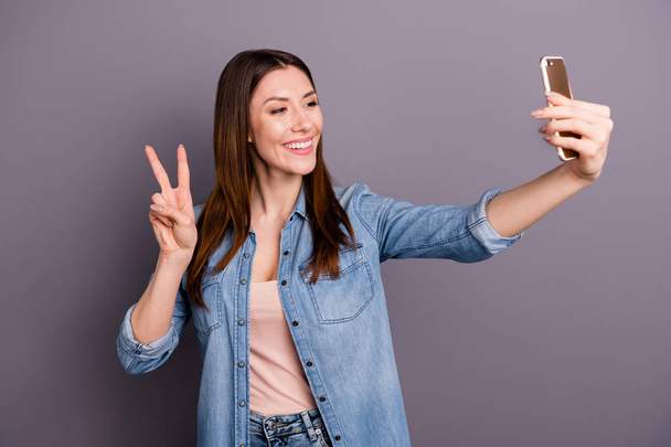 Πορτραίτο της θετικής εύθυμη γυναίκα πάρει selfie στο κινητό της έχουν κλήση βίντεο αισθάνονται περιεχόμενο κάνει v-πινακίδες για τις διακοπές της φορούν ντένιμ τζιν ρούχα απομονώνονται πάνω από γκρι χρώμα φόντου - Φωτογραφία, εικόνα
