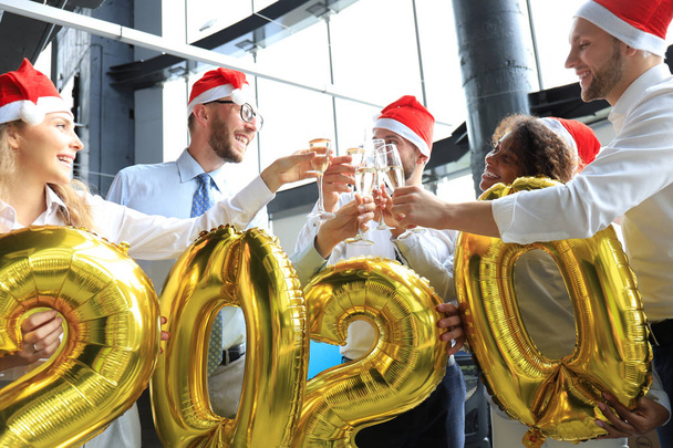 Pessoas de negócios estão comemorando férias no escritório moderno bebendo champanhe e se divertindo em co-working. Feliz Natal e Feliz Ano Novo 2020
. - Foto, Imagem