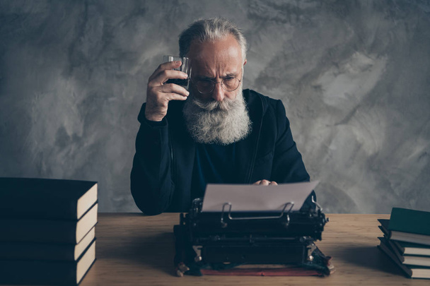 Portrait of his he nice attractive bearded gray-haired professional skilled creative publisher making screen life story novel drinking whiskey cognac over concrete wall background - Foto, Imagen