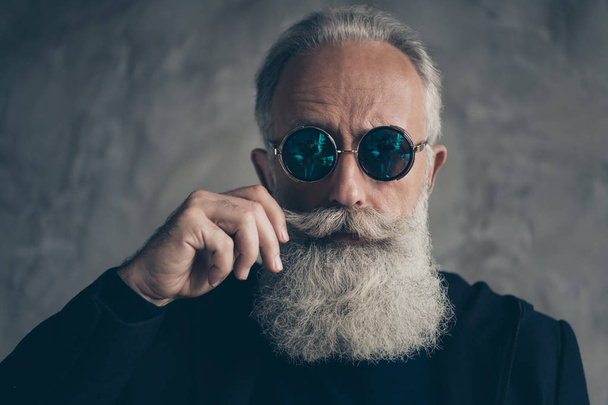 Close up photo of attractive harsh masculine pensioner in eyewear eyeglasses touching his moustache isolated over grey background - 写真・画像