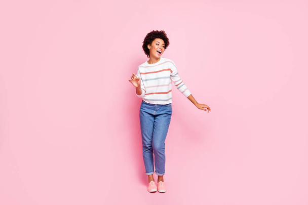 Full length photo of pretty dark skin lady at dancing party moving with favorite song rhythm wear striped pullover and jeans isolated pastel pink color background - Photo, image