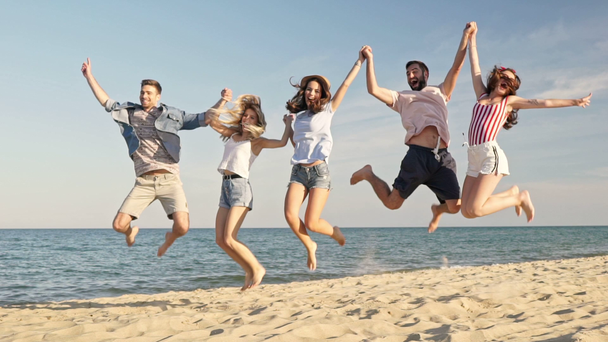 Група молодих веселих друзів посміхаються і стрибають разом, розважаючись на пляжі біля моря
 - Кадри, відео