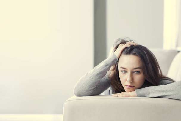 Depressed young woman on sofa at hom - 写真・画像
