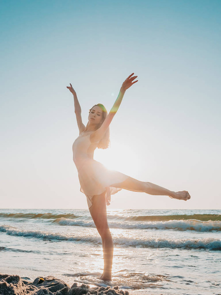 Karcsú szép balerina fehér ruhában táncoló balett a tengeren, vagy óceán homokos tengerpart a reggeli fényben. A művészet fogalma, természetszépség - Fotó, kép