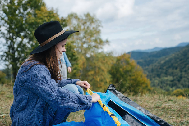 Kobieta przygotowuje swój niebieski namiot na zewnątrz patrząc na widok na góry. Camping dziewczyna w malowniczym krajobrazie korzystających wakacje podróży przygoda natury. Podróże, ludzie i koncepcja zdrowego stylu życia - Zdjęcie, obraz