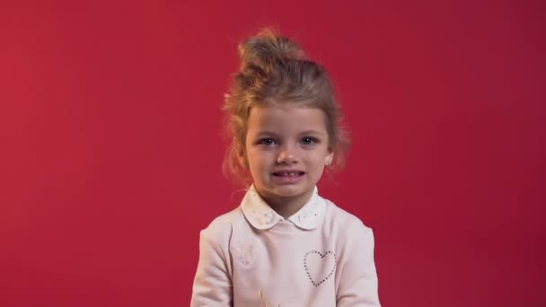 Close up of charming little girl with cute smile scattering confetti on the red background - Imágenes, Vídeo
