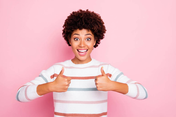 Photo of wavy curly cute cheerful nice funny black girl showing you thumb up with emotional face expression wearing white striped sweater isolated over pink pastel color background - 写真・画像