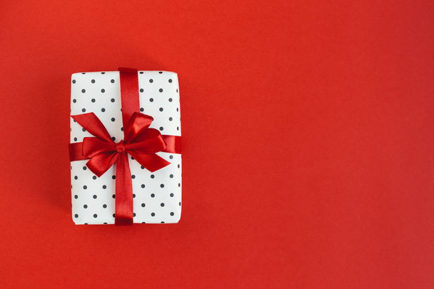 Gift box wrapped in black polka-dot white paper with red bow on red background. - Foto, Imagen