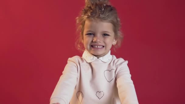 Close up of amazing happy little girl in white blouse with beautiful wrapped gift posing on camera on the red background - Кадры, видео