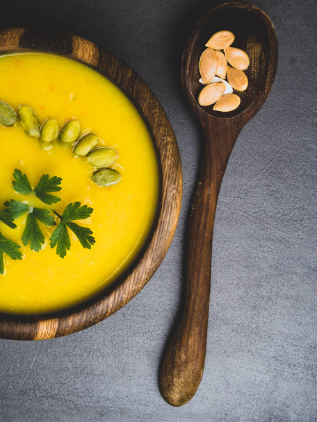 Тыквенный осенний суп в деревянной миске с петрушкой, семена, диетические овощные веганские продукты
 - Фото, изображение