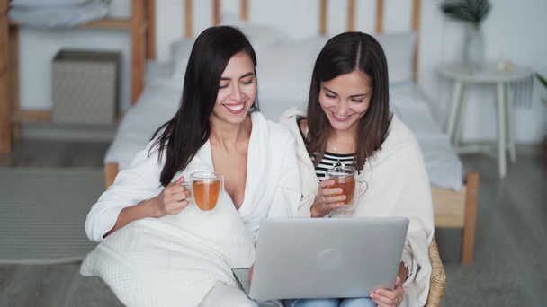 Two young women sisters at home watching comedy movie on laptop and drinking tea - Footage, Video