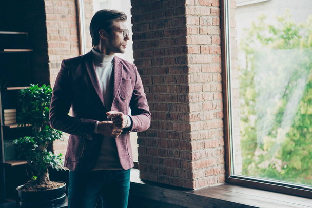 Photo of amazing business guy looking deeply thinking to window fixing clothes before corporate seminar wear specs stylish blazer turtleneck and jeans in modern office room - Zdjęcie, obraz