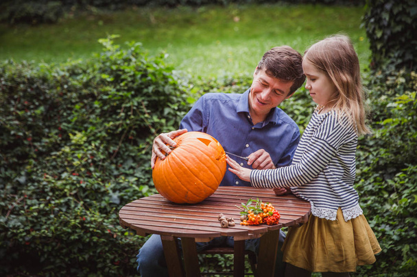 Hyvää halloweenia. Isä ja tytär veistämällä kurpitsa Halloween ulkopuolella
. - Valokuva, kuva