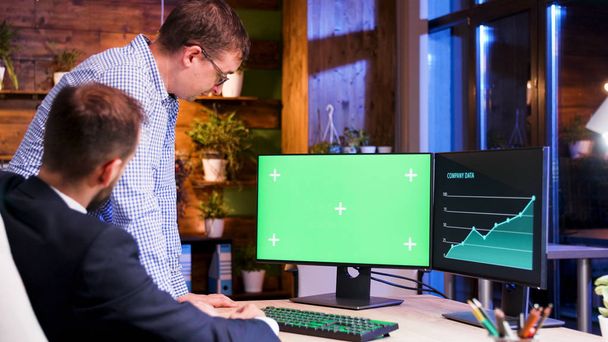 緑色のコンピュータ画面を見ている 2 人のオフィスの同僚 - 写真・画像