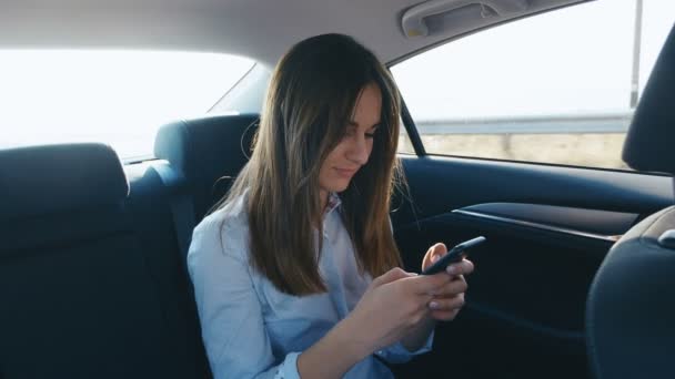 Portret młoda kobieta za pomocą smartfona podczas podróży samochodem z kierowcą. Dziewczyna jest sprawdzanie maili, czaty, podczas gdy ona jeździ w taksówce - Materiał filmowy, wideo