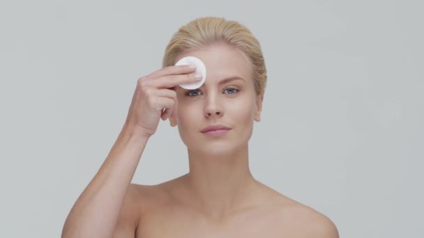 Studio portrait of young, beautiful and natural blond woman applying skin care cream. Face lifting, cosmetics and make-up. - Video