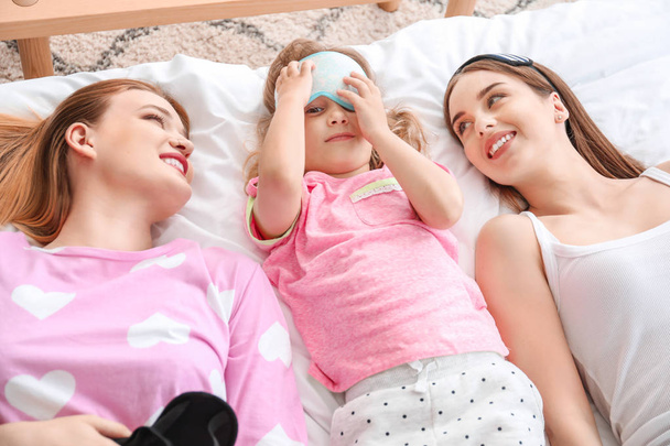 Happy lesbian couple with little daughter lying on bed - Photo, image