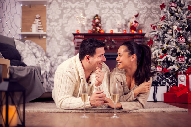 クリスマスの日にリビングルームに横たわる手をつないでいる若い夫婦 - 写真・画像