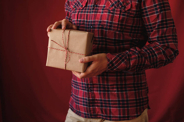 Man in plaid shirt holding Christmas box Gift on red background. Male hands with Presents for winter Holidays. Christmas, New Year, shopping, preparation on Holidays concept. Close up - Photo, image