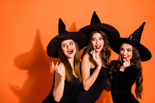 Photo of three cruel witch ladies calling handsome guys using paranormal magic powers wear black dresses and wizard hats isolated orange color background - Fotoğraf, Görsel
