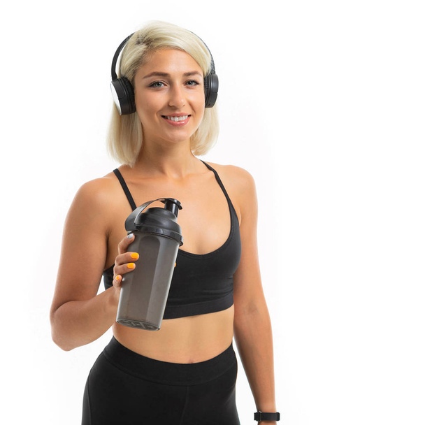 νεαρή όμορφη ξανθιά αθλήτρια με ακουστικά και μπουκάλι νερό - Φωτογραφία, εικόνα