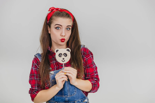 Funny young girl standing with yummy panda-lollipop in her hand, making duck face. - Fotoğraf, Görsel