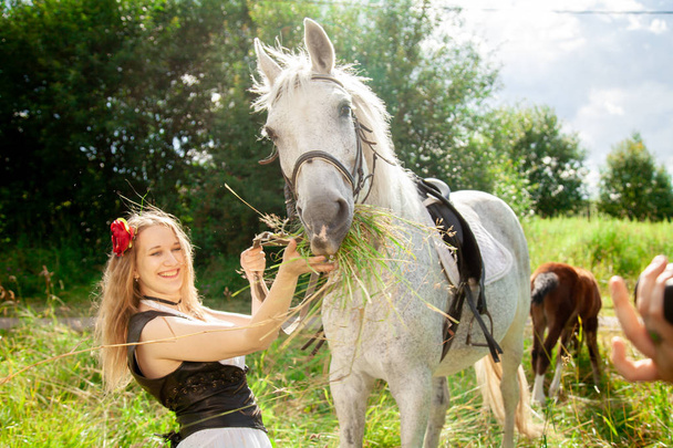 Hermosa chica joven caucásica caminando con un caballo y disfruta del verano en el campo
. - Foto, imagen