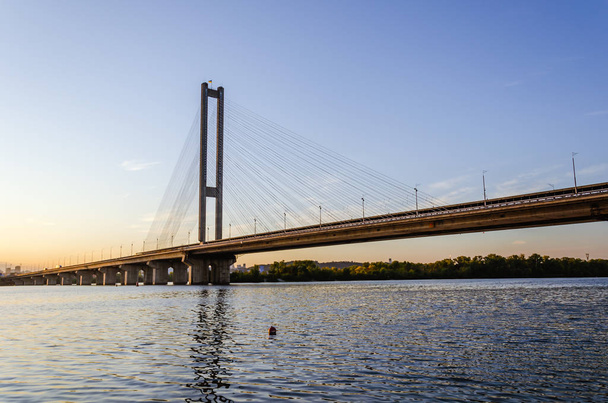 Most południowy, Kijów, Ukraina. Kijów most nad rzeką Dniepropietrowsku na tle pięknego zachodu słońca. Most w wieczornym słońcu - Zdjęcie, obraz