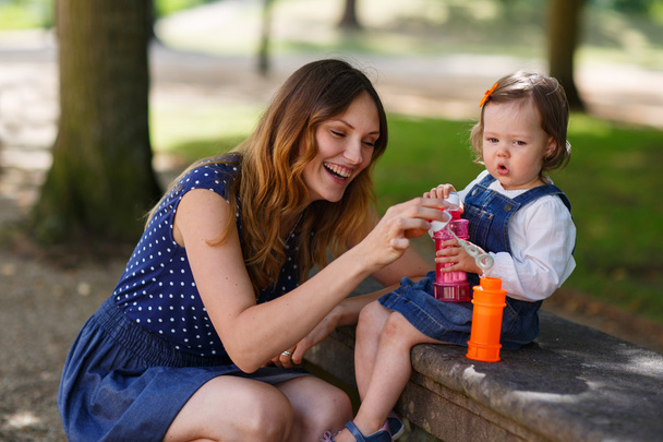 Beautiful mother and little daughter blowing soap bubbles in sum - 写真・画像