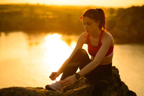 junge Sportlerin schnürt Laufschuhe und bereitet sich auf den Trailrun bei Sonnenuntergang vor. gesunder Lebensstil und Sportkonzept. - Foto, Bild