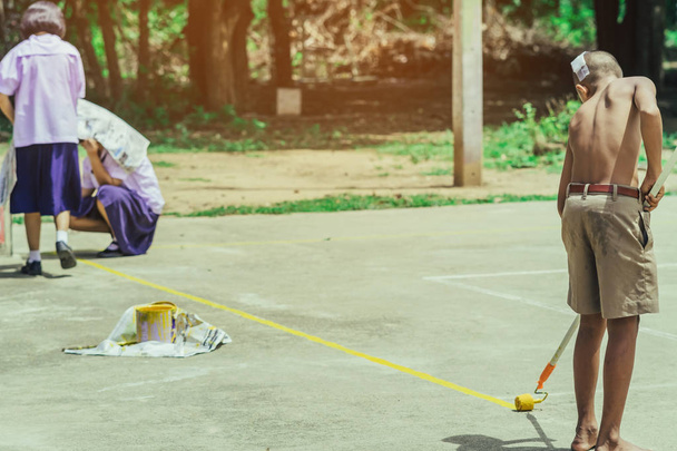 Los estudiantes masculinos usan pequeños rodillos de pintura para pintar líneas amarillas en el suelo de cemento para el entrenamiento Sepak Takraw.
. - Foto, imagen