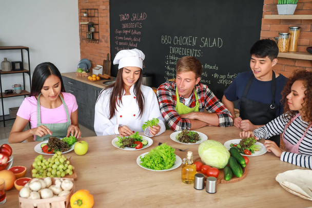 Naiskokki ja ryhmä nuoria ruoanlaittokursseilla
 - Valokuva, kuva