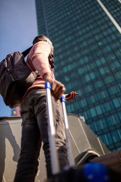 Portrait de derrière jeune homme debout dehors en ville avec téléphone portable et sacs de voyage
 - Photo, image