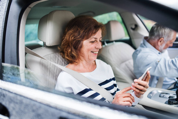 Happy senior couple with smartphone sitting in car, going on trip. - Zdjęcie, obraz