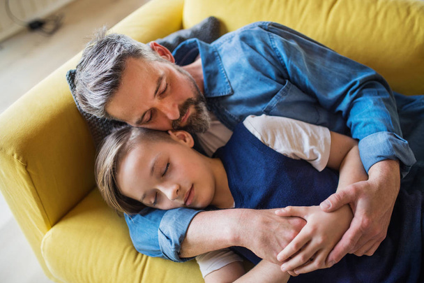 Mature father with small son lying on sofa indoors, sleeping and resting. - Valokuva, kuva
