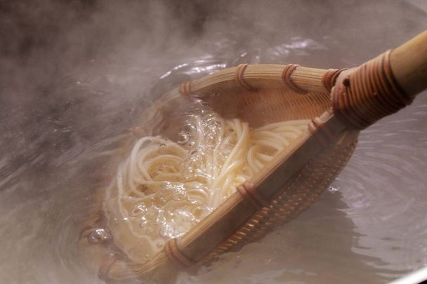 The bamboo pole picks up the hot noodles in the cauldron, and the noodle teeth have an appetite - Photo, Image